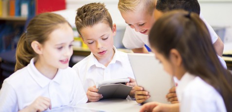Happy students in classroom using a digital tablet, they are all wearing uniforms.
