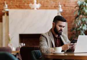 Mies lukee viestiä tabletista kannettavan tietokoneen äärellä